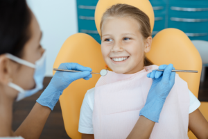 A child sitting in a chair with a dentist holding a mirror