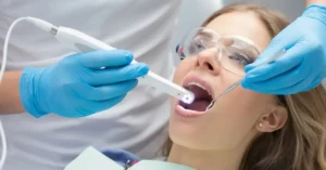 Female patient receiving a dental exam with an intraoral camera and mirror, performed by a gloved dentist in a clinical setting, illustrating modern preventive dentistry techniques.