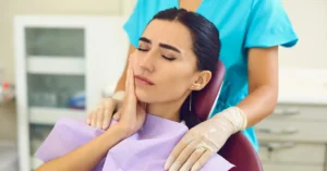 Female patient in a dental chair holding her jaw in discomfort, being comforted by a dentist, depicting wisdom tooth pain or discomfort.